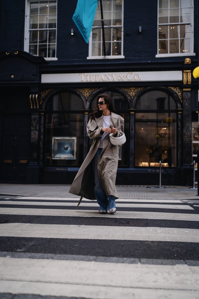 A woman walking across a street holding a blue umbrella